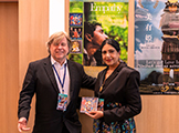 Filmmaker Francisco Bassignana and Host & Jury Member Sumathy Ram in front of the Official Poster Out-Of Competition Premiere EMPATHY a powerful srory and music video